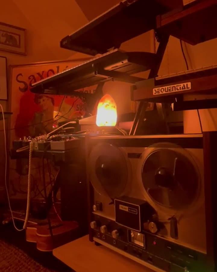 Reel-to-reel tape machine beneath stacked studio synthesizers